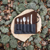 Set of cutlery in a leather case on a wooden surface surrounded by natural elements.